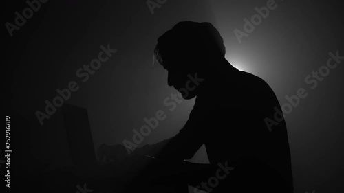 Silhouette of computer hacker in hoodie with laptop in dark