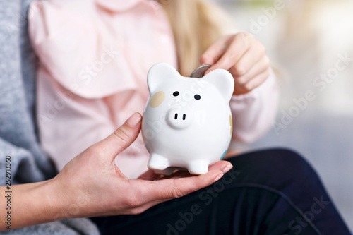Young girl and her mother with piggybank sitting at table