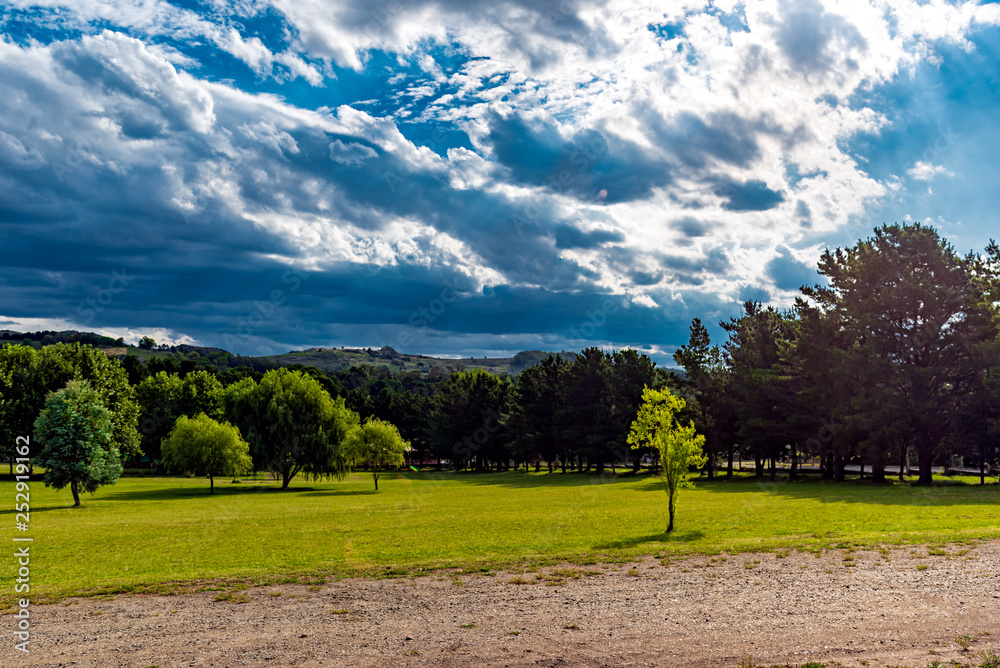 Obraz premium Landscape with mountains on the back, a lot of trees, green grass and a road in the front on a cloudy day with sunrays on the image