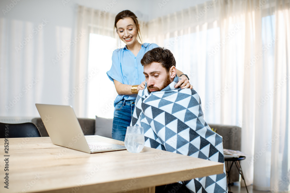 Young woman taking care giving some medicine for a man feeling sick covered with blanket at home Young woman taking care giving some medicine for a man feeling sick covered with blanket at home