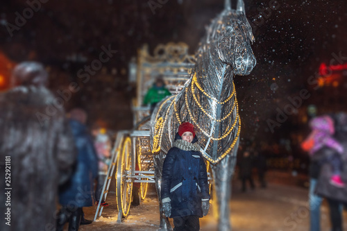 Little girl in winter stands near the statue of a glowing horse