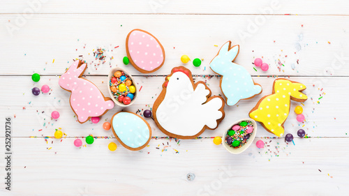 Easter greetings card with colorful gingerbread and sweets. On a white wooden background. Top view. Free space for your text.