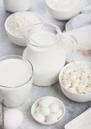 Fresh dairy products on white table background. Jar and glass of milk, bowl of sour cream, cottage cheese and baking flour and mozzarella. Eggs and cheese.