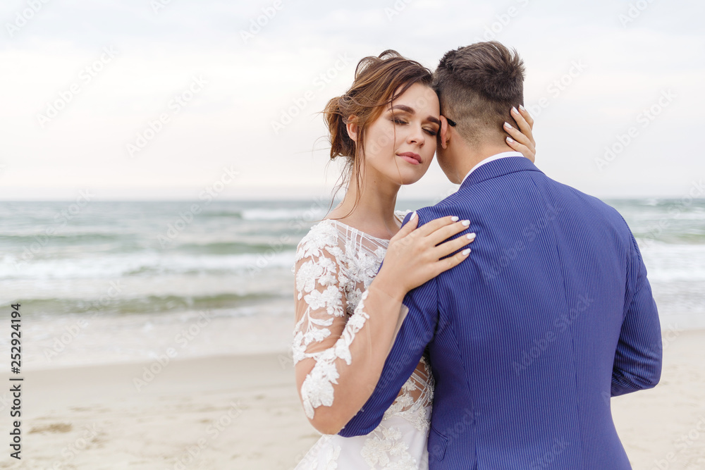 newlyweds walking along the sea beach at the wedding. The groom hugs the bride newlyweds walking along the sea beach at the wedding. The groom hugs the bride