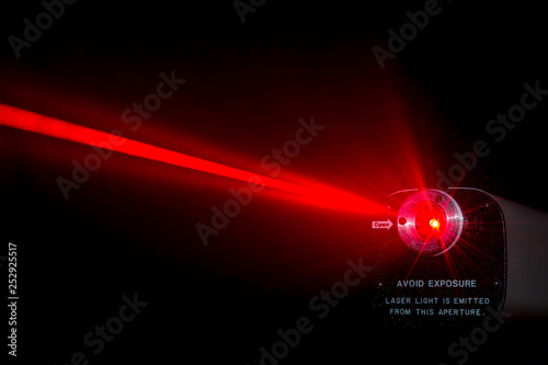 Red laser beam from a lab laser. Warning notice on front. Black background. Beam scatters near aperture.