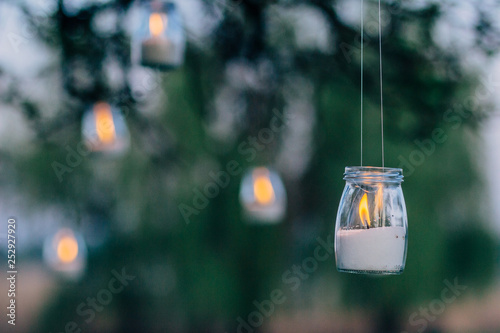 The lamp made of a jar with a candle is hanging on a tree at night. Wedding night decor.