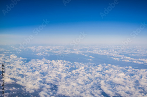 View from a plane window on clouds and blue clear sky and the earth from height. Beautiful view from air of mountains.  © Vlada