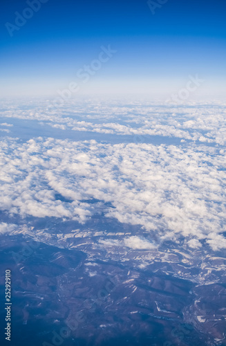 View from a plane window on clouds and blue clear sky and the earth from height. Beautiful view from air of mountains. 