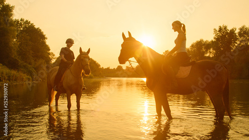 SUN FLARE: Morning sun rays shine on the women riding horses along the stream.