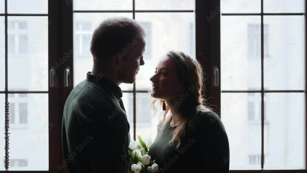 Pregnant family young husband and wife silhouette tenderly kissing by window Pregnant family young husband and wife silhouette tenderly kissing by window