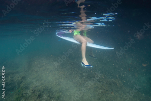 Surf girl sitting on a surfboard with shoes underwater