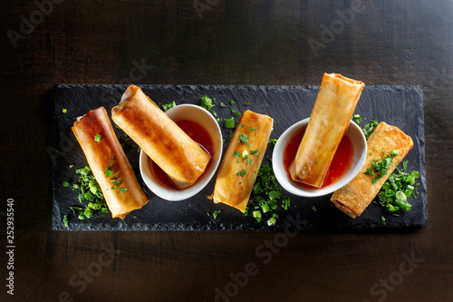 Fried spring rolls on black slate decorated with greens.