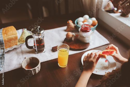 happy kid girl having breakfast at home, eating toast with jam and eggs on farmhouse kitchen