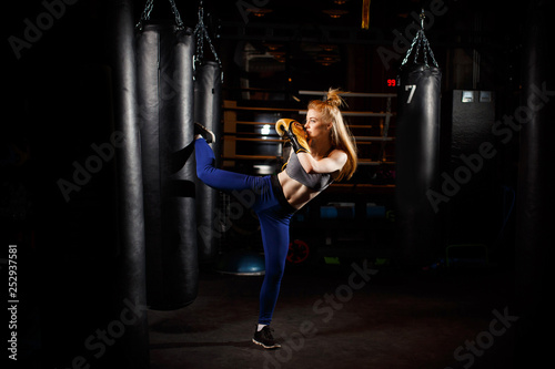 Blonde in boxing gloves kicks black bag. © snedorez