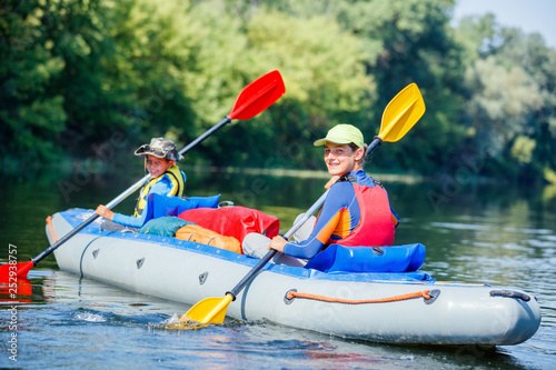 Happy kids kayaking on the river on a sunny day during summer vacation