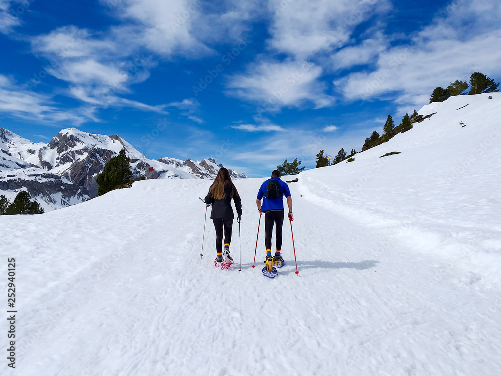 couple of excursionists walking on snowshoes and stick poles on the white snow of the winter of a path of a snowy mountain