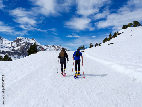 couple of excursionists walking on snowshoes and stick poles on the white snow of the winter of a path of a snowy mountain