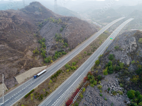 Aerial view of elevated highway thru dry mountain. Highway over the mountain with cars and trucks driving both direction. Open road, freeway in dry landscape. Chengde, China.