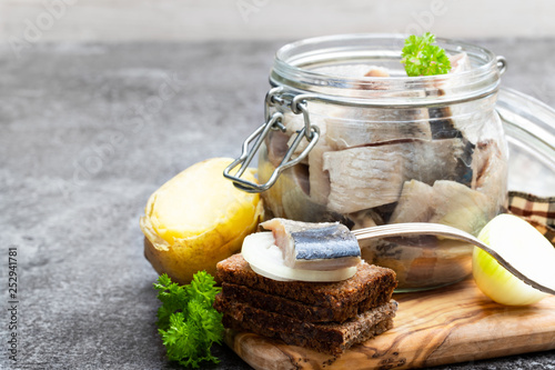 Quadro em tela Homemade marinated herring in glass jar with rye bread and jacket potato on gray