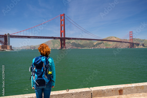 Young woman wearing backpack is watching Golden Gate bridge from the pier in San Francisco, United States on America