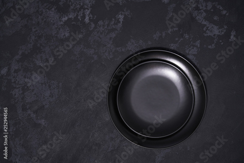 Two empty black plates on a black background, top view.