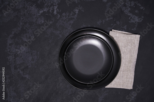 Two empty black plates and napkin on a black background, top view.
