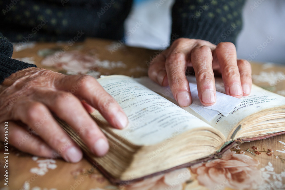 Old woman hands on the open prayer book.