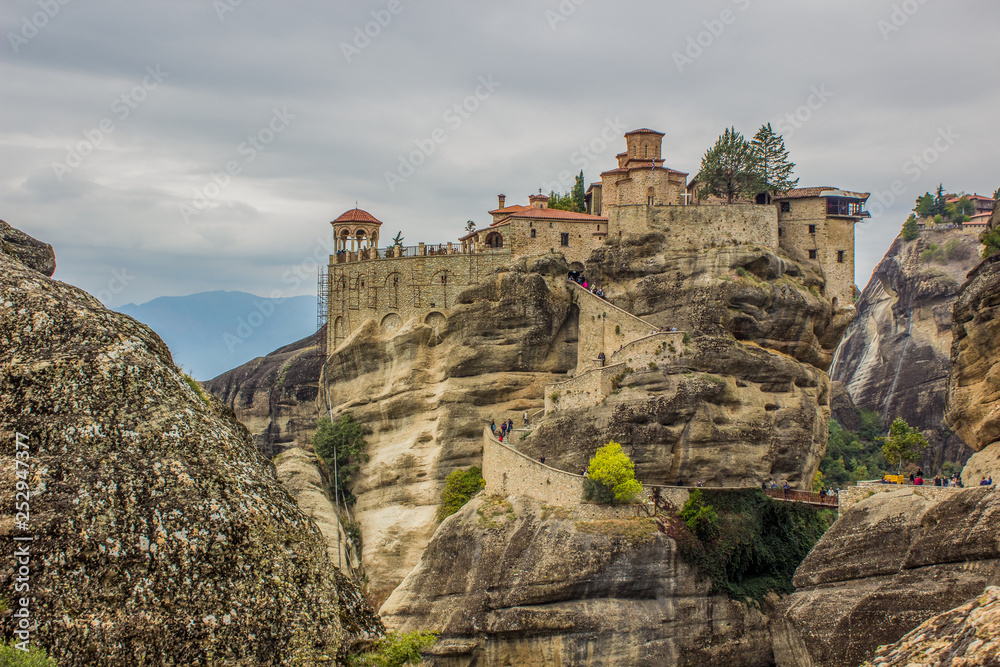 picturesque highland mountain monastery ancient religion building on top of steep rock holy place for pilgrims in Greece, cloudy sky dramatic background