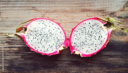 Juicy pink pitaya cut in two pieces on wooden table closeup
