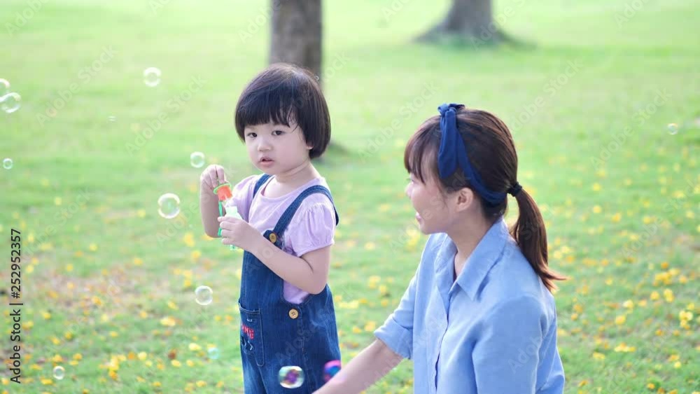 Asian family with Mother and daughter or children Girl playing blow soap bubbles having fun in nature park and sunlight. Slow Motion Asian family with Mother and daughter or children Girl playing blow soap bubbles having fun in nature park and sunlight. Slow Motion