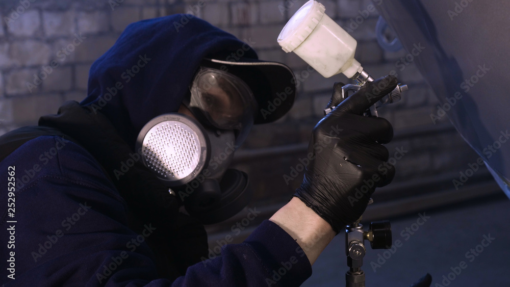 A professional guy (man) in the garage covers the yacht (transport) with a mini-jet (sprays) by applying paint (ceramics) to the surface using a protective suit dispenser and protective glasses.