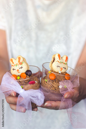 Woman's hands holding transparent plastic cup with chocolate mousse, decorated with bunny shaped cookie