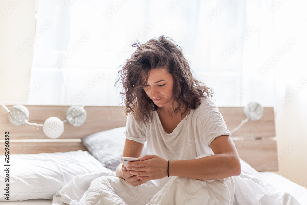 A smiling woman holds her phone in front of her on the bed A smiling woman holds her phone in front of her on the bed