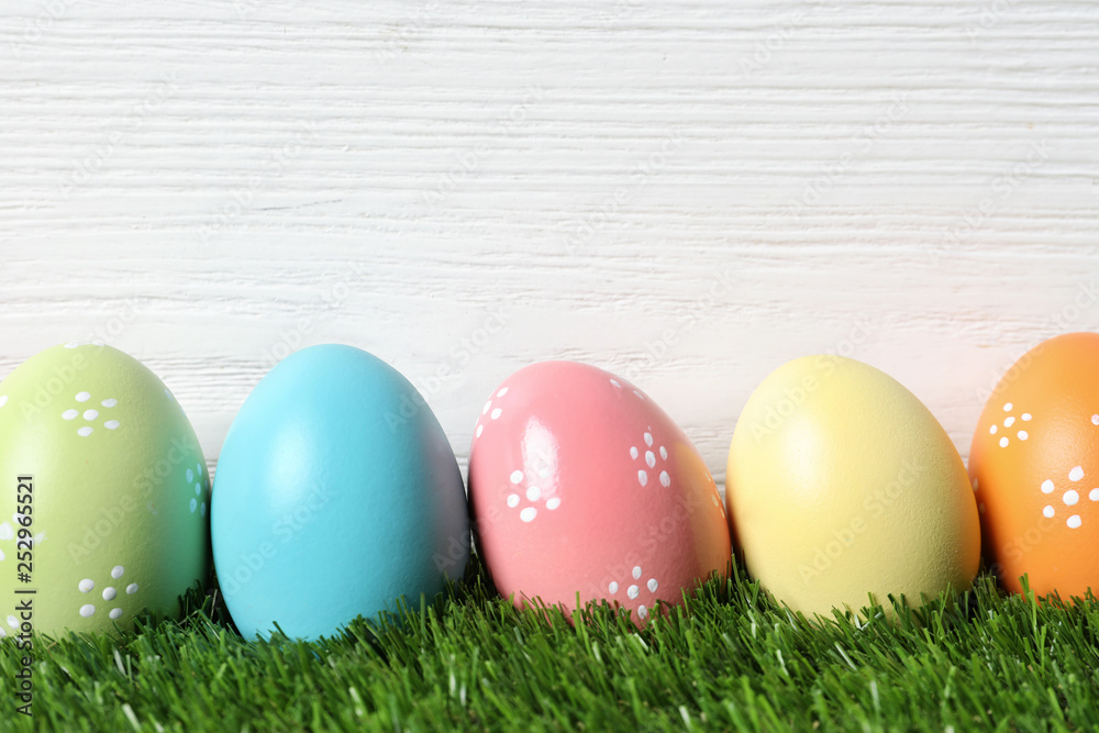 Colorful painted Easter eggs on green grass against wooden background, space for text