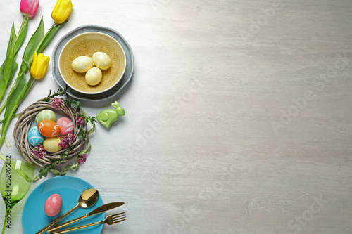 Festive Easter table setting with painted eggs on wooden background, top view. Space for text