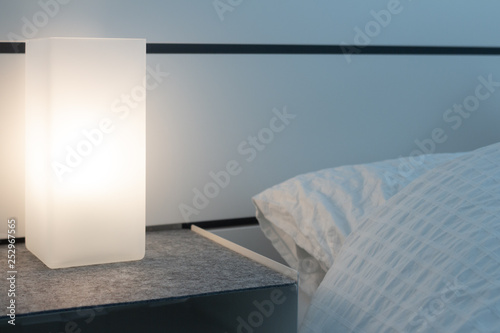 Modern square lamp on a nightstand lighting up a dark bedroom