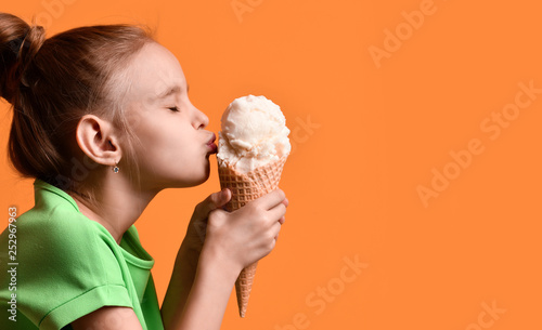 Fotografia, Obraz Little baby girl kid kissing vanilla ice cream in waffles cone on yellow orange