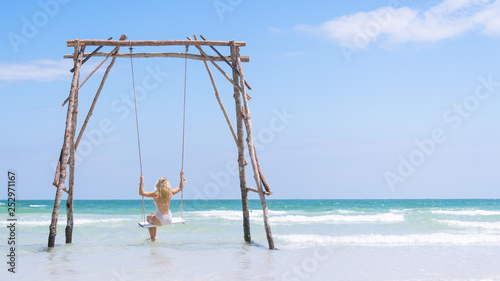 Beautiful Young Blonde Traveler Girl in a white swim suit, Swinging on a Sea Swing Framed off to the left in Phu Quoc Island, Vietnam