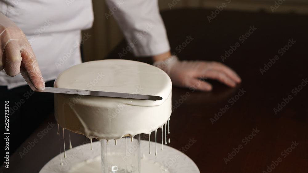 Confectioner fills cakes with white liquid glaze. She equals top surface of cake. Excess cream drains from baking. Confectioner fills cakes with white liquid glaze. She equals top surface of cake. Excess cream drains from baking.