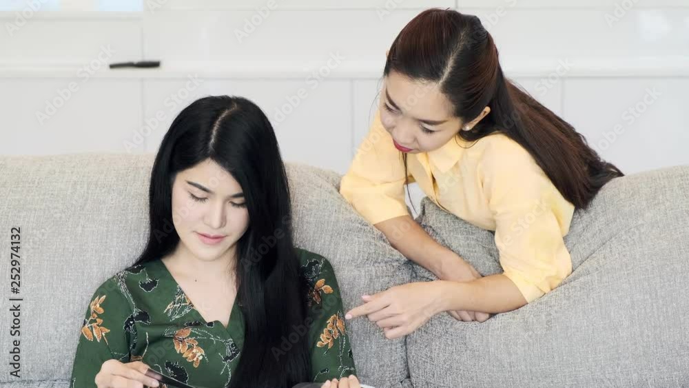 Young beautiful asian woman reading book on couch and talking to her mother in living room, smiling. Young woman relationship concept. Young beautiful asian woman reading book on couch and talking to her mother in living room, smiling. Young woman relationship concept.