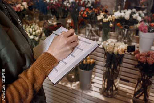 Girl writes in a notebook about a flower's shop. Management. Business writing. Woman hands write to the notebook about the flowers. Detail. Close up.