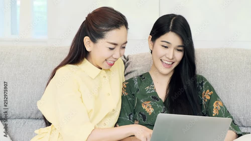 Young beautiful asian woman browsing internet on laptop with her mother on a couch, having fun. Young woman relationship concept. Young beautiful asian woman browsing internet on laptop with her mother on a couch, having fun. Young woman relationship concept.