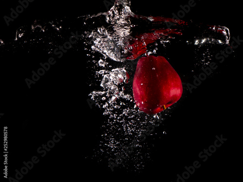 red apple , yellow lemon falling into splashing water on black background