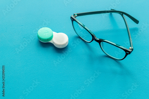Eye problems. Glasses with transparent lenses and contact lenses on blue background copy space