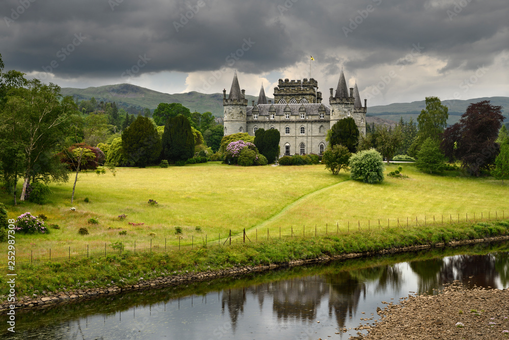 Inveraray Castle reflected in the River Aray at Loch Fyne with dark clouds and golden grass in the Scottish Highlands Scotland UK