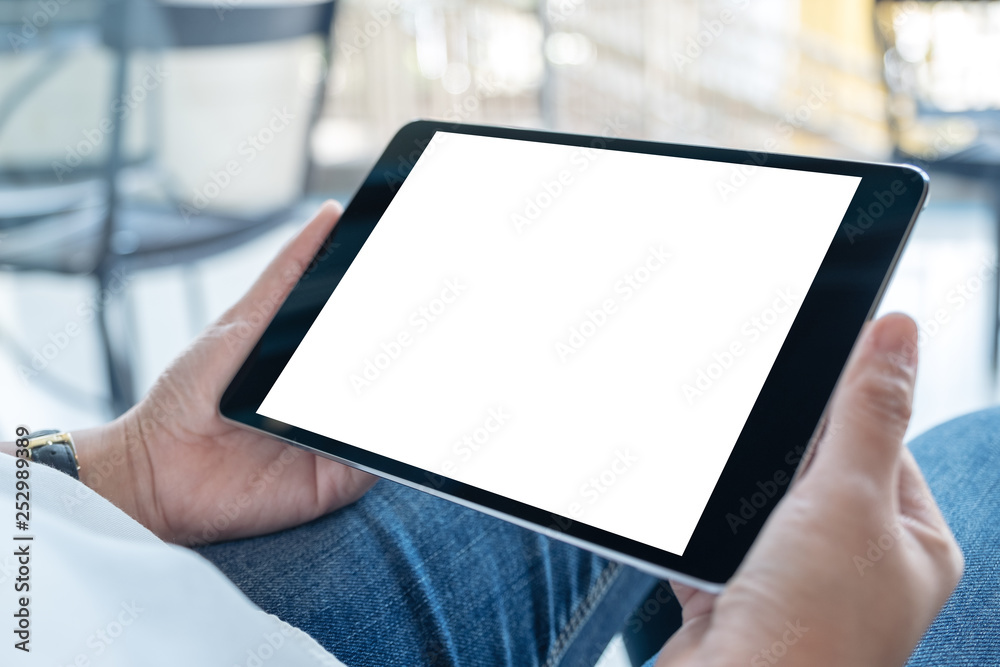 Fototapeta premium Mockup image of a woman holding black tablet pc with blank white screen horizontally while sitting in cafe
