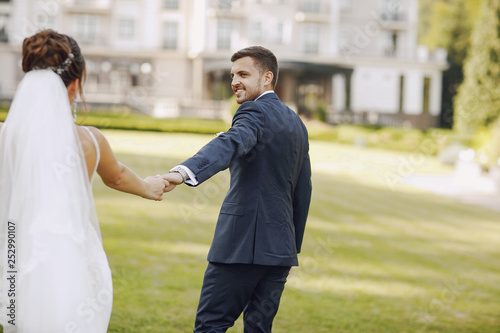 A young and beautiful bride and her husband is standing in a summer park with bouquet of flowers