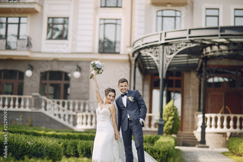 A young and beautiful bride and her husband is standing in a summer park with bouquet of flowers