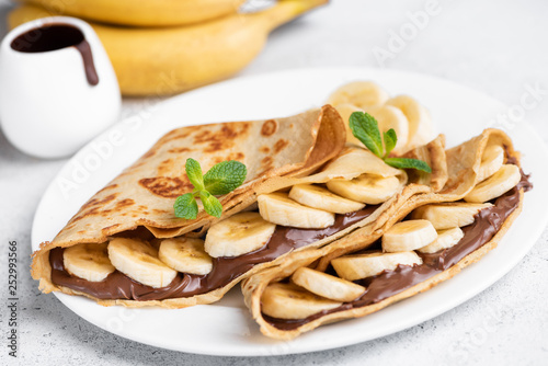 Crepes stuffed with chocolate spread and banana on white plate. Thin pancakes, blini. Sweet dessert. photo