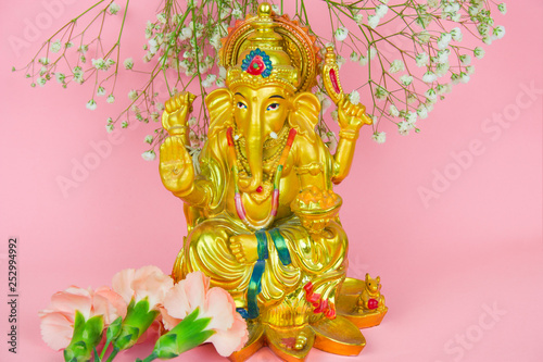 Lord Ganesha and flowers statuette on a vibrant pink background